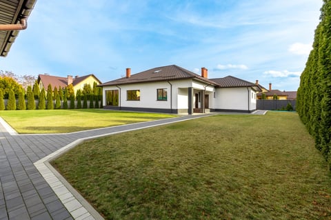A modern suburban house with a brown roof, large green lawn, and a paved walkway