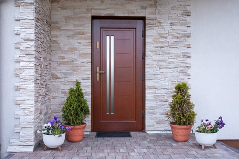 A front door detail with a stone accent wall, a brown door, covered porch, white posts and railing, and white siding