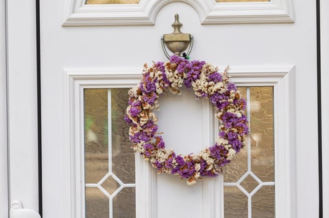 Decorative purple and white dried flower wreath hanging on a white front door with textured glass panels