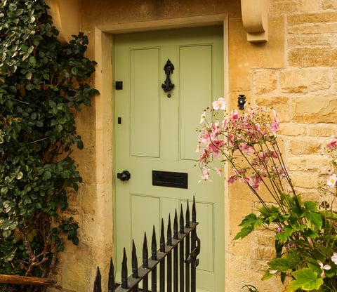 Charming British home facade with a pastel green door, decorative iron features, and lush foliage, evoking classic elegance