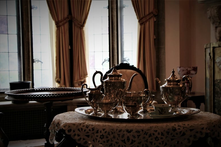 Ornate gold tea set displayed on decorative table with brown curtains and grand piano in elegant room